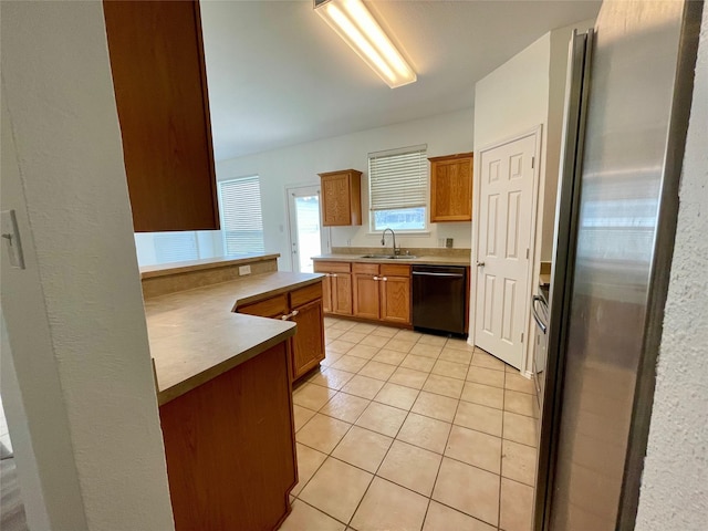 kitchen featuring light tile patterned floors, a sink, freestanding refrigerator, brown cabinets, and dishwasher