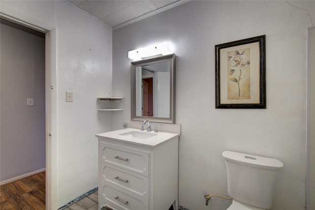 half bathroom with crown molding, vanity, toilet, and wood finished floors