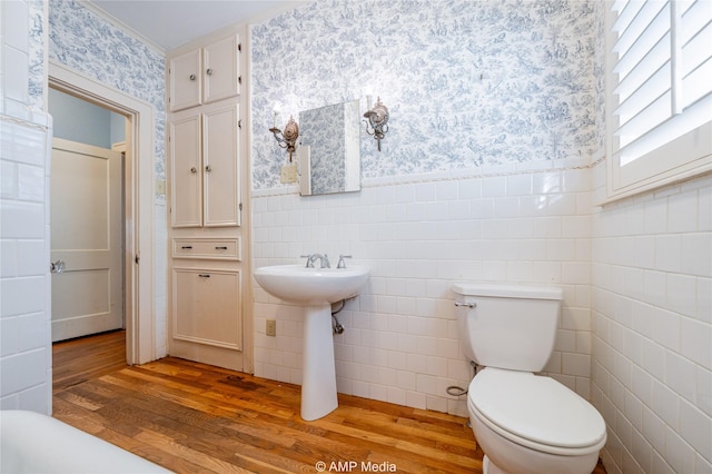 bathroom featuring wallpapered walls, wainscoting, toilet, wood finished floors, and tile walls