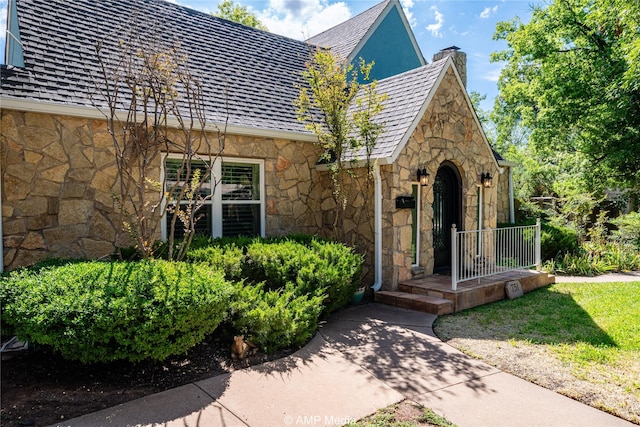 view of front facade with a high end roof, stone siding, and a chimney