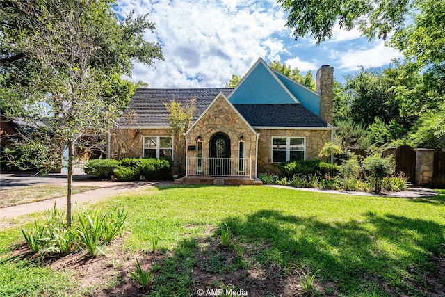 tudor-style house featuring a front yard, stone siding, and a chimney