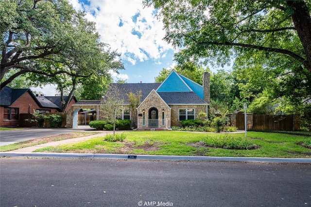 view of front of property featuring fence, driveway, stone siding, a chimney, and a front yard