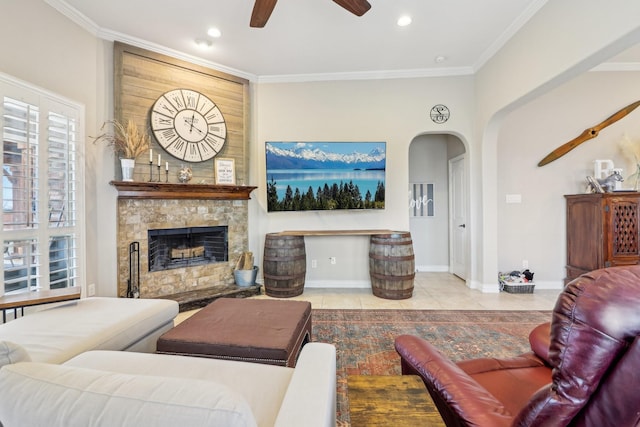 living area featuring ceiling fan, a stone fireplace, light tile patterned flooring, baseboards, and ornamental molding