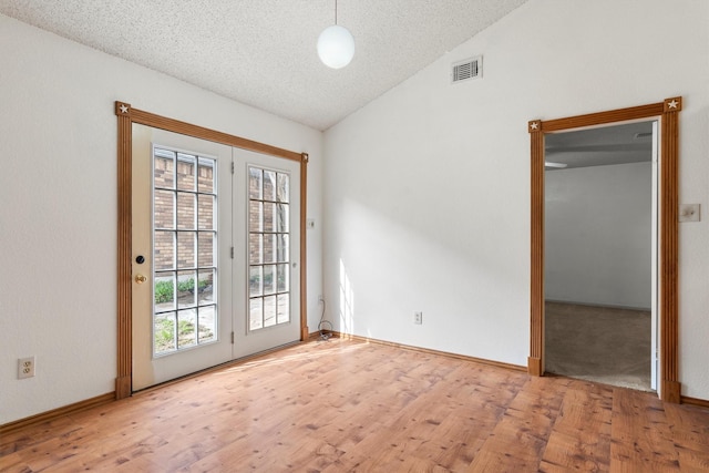 doorway to outside with visible vents, a textured ceiling, wood finished floors, baseboards, and lofted ceiling