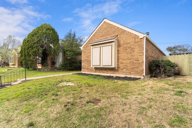 view of property exterior featuring a yard, fence, and brick siding