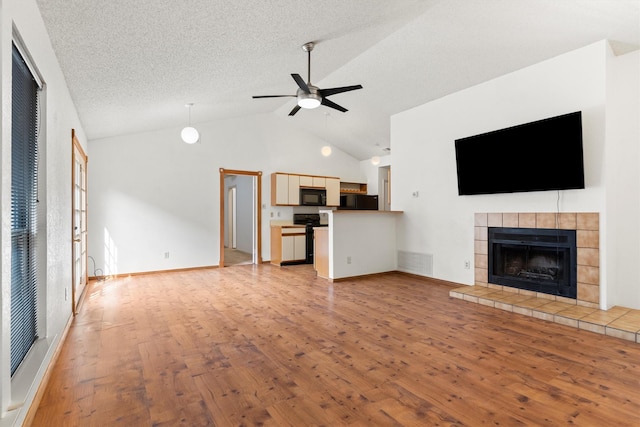 unfurnished living room with visible vents, vaulted ceiling, a tile fireplace, light wood-style floors, and a ceiling fan