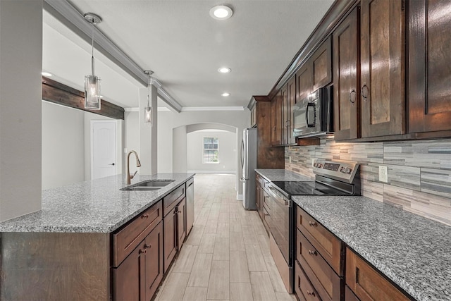 kitchen featuring arched walkways, dark stone counters, appliances with stainless steel finishes, decorative light fixtures, and a sink