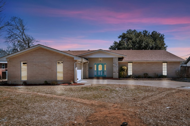 view of front of house with a garage, concrete driveway, brick siding, and roof with shingles