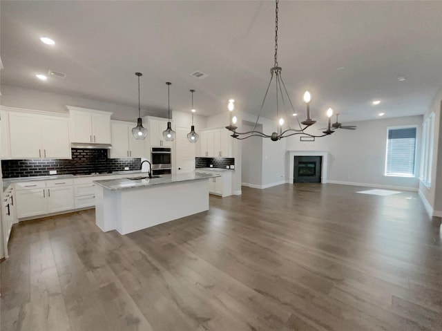 kitchen with wood finished floors, a sink, open floor plan, backsplash, and an island with sink