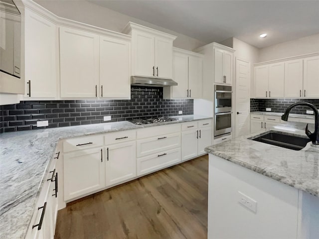 kitchen with appliances with stainless steel finishes, wood finished floors, under cabinet range hood, white cabinetry, and a sink