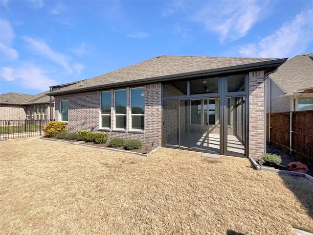 back of house with brick siding, a shingled roof, fence, and a sunroom