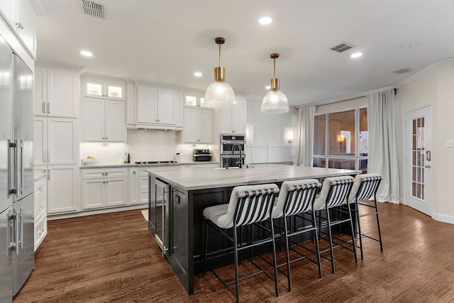 kitchen with visible vents, hanging light fixtures, glass insert cabinets, a kitchen island with sink, and white cabinets