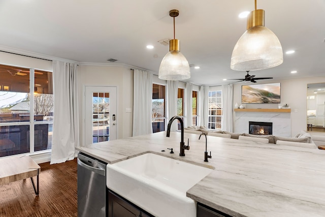 kitchen with open floor plan, light stone countertops, stainless steel dishwasher, pendant lighting, and a sink