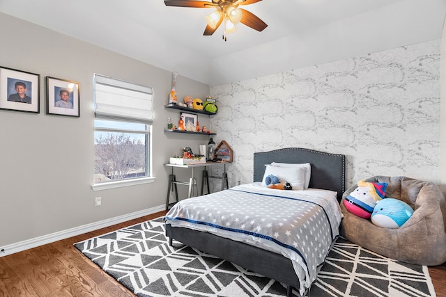 bedroom featuring baseboards, lofted ceiling, ceiling fan, an accent wall, and wood finished floors