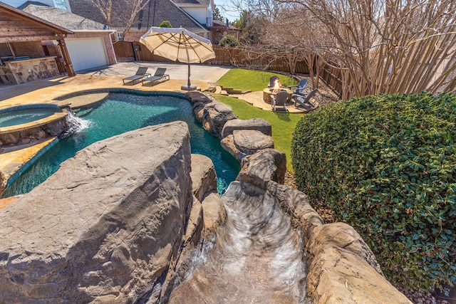 view of swimming pool featuring a pool with connected hot tub, a fenced backyard, an outdoor fire pit, a patio area, and an outdoor bar