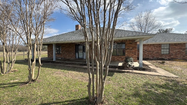 rear view of house featuring a shingled roof, brick siding, a lawn, and a chimney