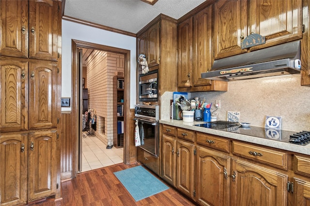 kitchen with light countertops, wood finished floors, oven, under cabinet range hood, and black electric cooktop