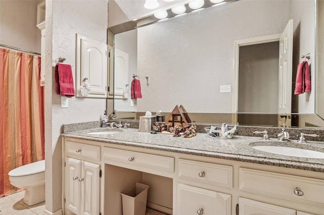 bathroom featuring double vanity, toilet, a sink, and a textured wall