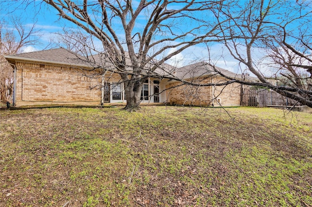 rear view of property featuring roof with shingles, brick siding, and a lawn