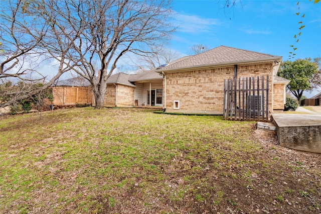 rear view of property featuring a shingled roof, brick siding, fence, and a lawn