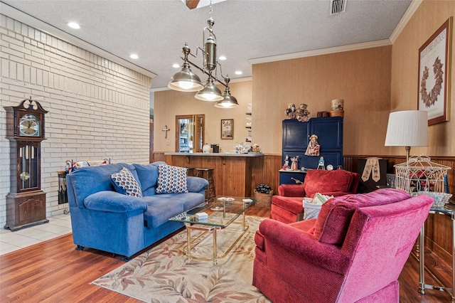 living room with visible vents, a wainscoted wall, light wood-style flooring, crown molding, and a textured ceiling