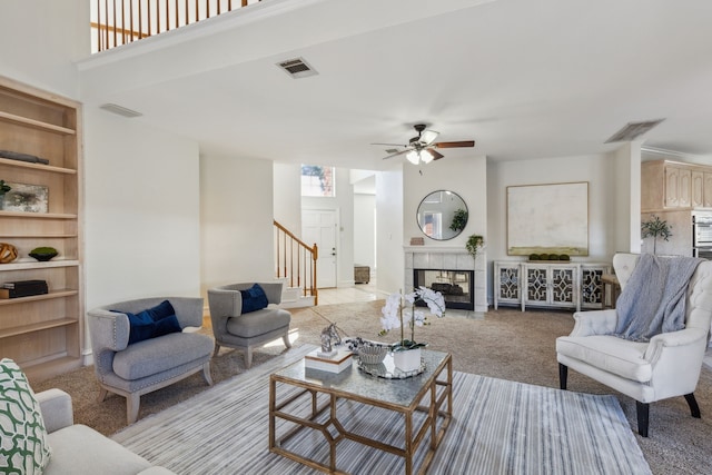 living area with light carpet, stairway, a tiled fireplace, and visible vents