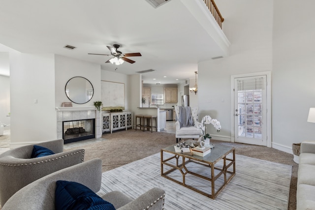 living room featuring a fireplace, visible vents, light carpet, baseboards, and ceiling fan with notable chandelier