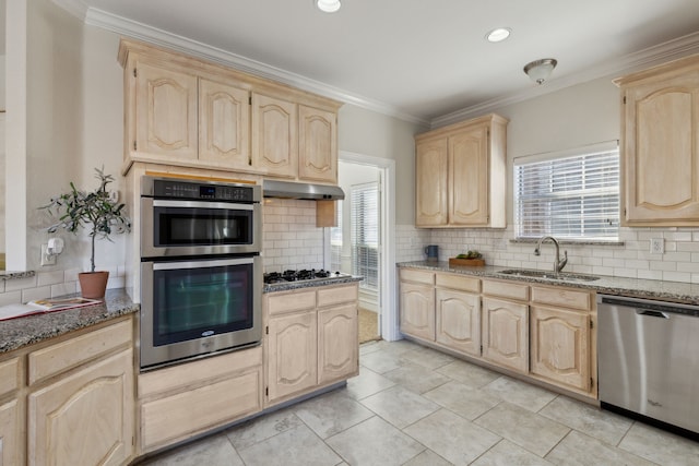 kitchen with light brown cabinets, under cabinet range hood, a sink, appliances with stainless steel finishes, and dark stone countertops