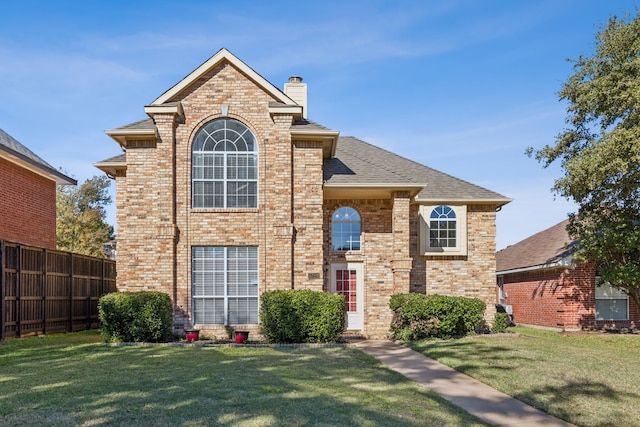 traditional home featuring brick siding, a chimney, fence, and a front yard