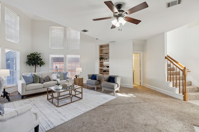 living area with baseboards, stairway, visible vents, and light colored carpet