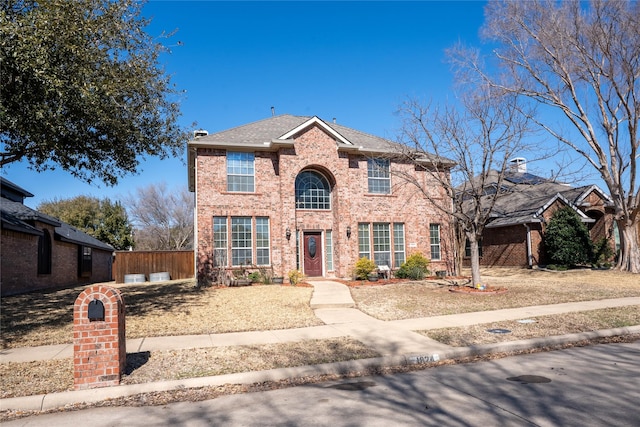 traditional-style house featuring roof with shingles, fence, and brick siding