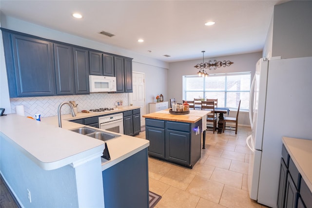 kitchen featuring white appliances, butcher block counters, a breakfast bar area, a peninsula, and a sink