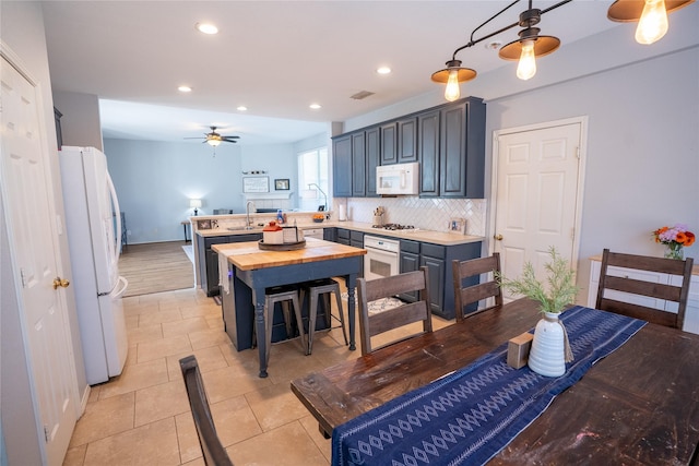 kitchen with white appliances, decorative backsplash, butcher block countertops, a peninsula, and a sink