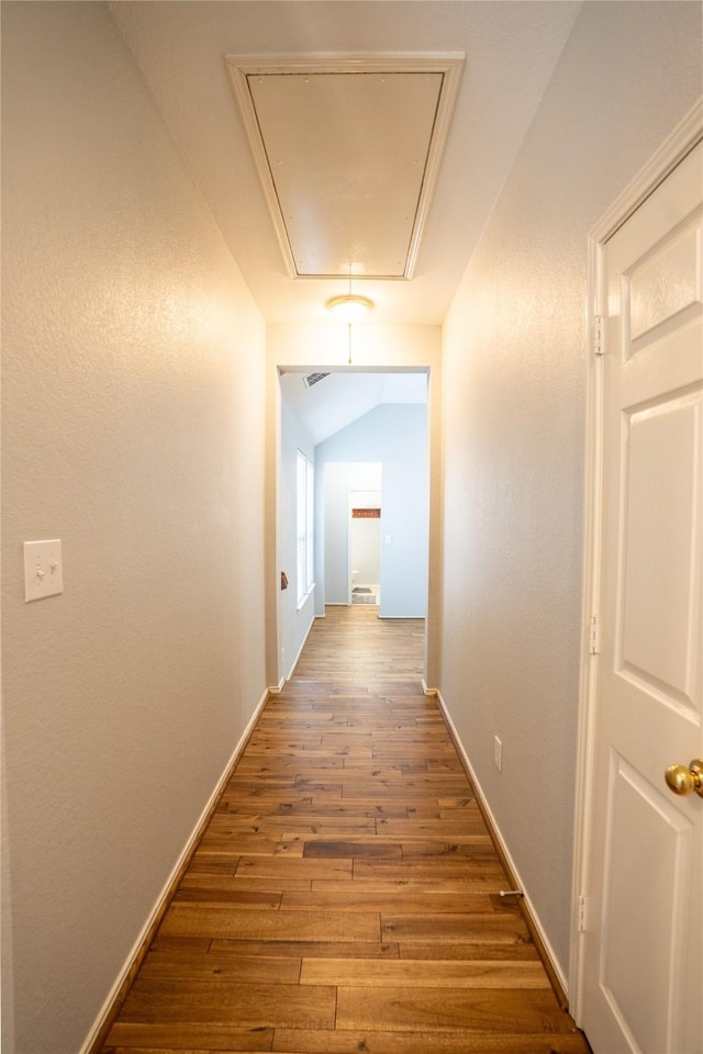 hall featuring lofted ceiling, attic access, baseboards, and wood finished floors