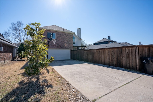 view of home's exterior featuring a garage, concrete driveway, brick siding, and fence