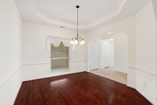 spare room with a chandelier, light wood-type flooring, a raised ceiling, and crown molding