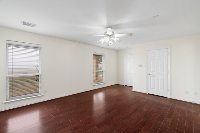 unfurnished room with dark wood-style floors, visible vents, baseboards, and a ceiling fan