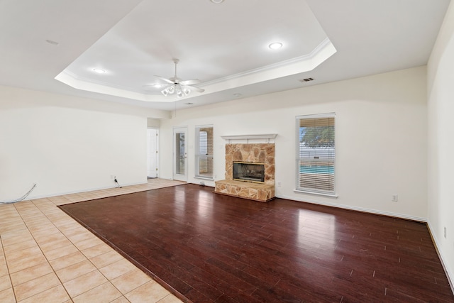 unfurnished living room with ornamental molding, a raised ceiling, ceiling fan, and a stone fireplace