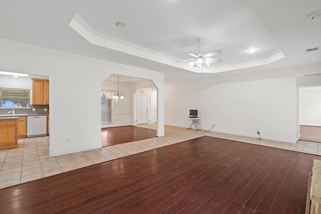 unfurnished living room with light wood-style floors, visible vents, and a tray ceiling