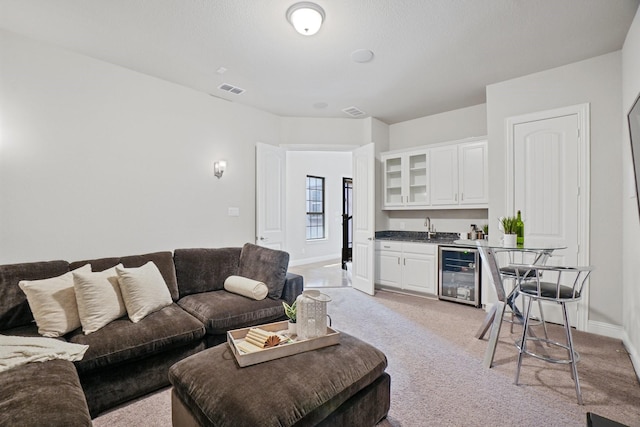 living room with wine cooler, light carpet, visible vents, baseboards, and wet bar