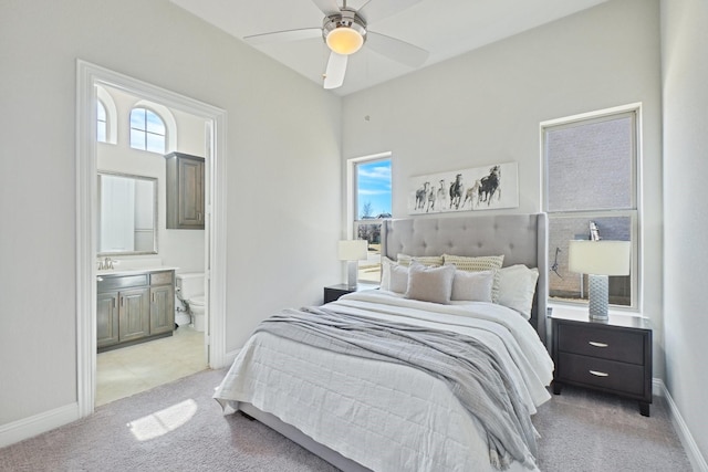 bedroom featuring light colored carpet, ensuite bathroom, baseboards, and multiple windows