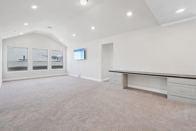 unfurnished living room featuring lofted ceiling, built in desk, baseboards, and light colored carpet