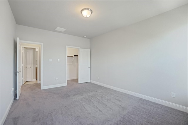 unfurnished bedroom with baseboards, a closet, a walk in closet, and light colored carpet