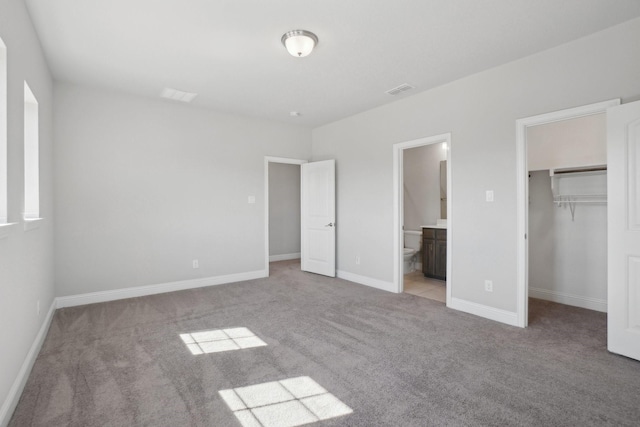 unfurnished bedroom featuring connected bathroom, light colored carpet, baseboards, a closet, and a walk in closet