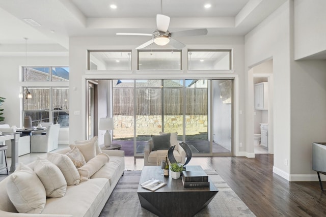 living area featuring dark wood-style floors, ceiling fan, a raised ceiling, and baseboards