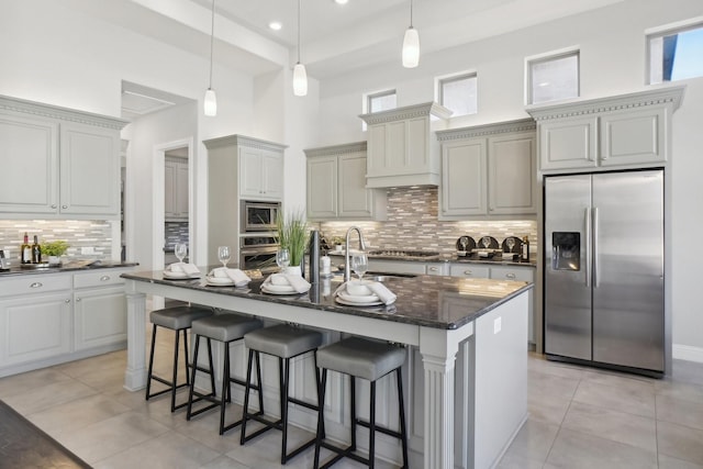 kitchen featuring light tile patterned floors, appliances with stainless steel finishes, an island with sink, and decorative light fixtures