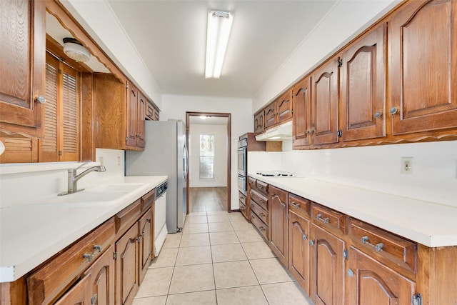 kitchen with brown cabinets, light tile patterned floors, light countertops, white dishwasher, and under cabinet range hood