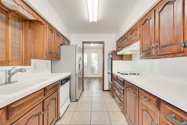 kitchen featuring white appliances, brown cabinets, light countertops, under cabinet range hood, and a sink