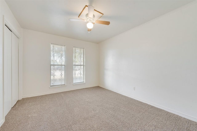 carpeted empty room with ceiling fan, baseboards, and crown molding