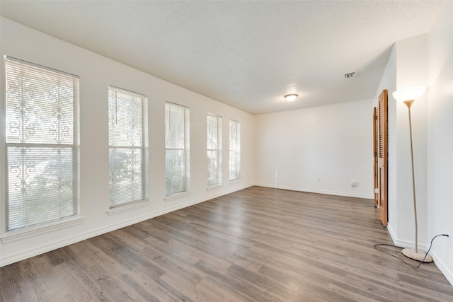 unfurnished room featuring visible vents, a textured ceiling, baseboards, and wood finished floors